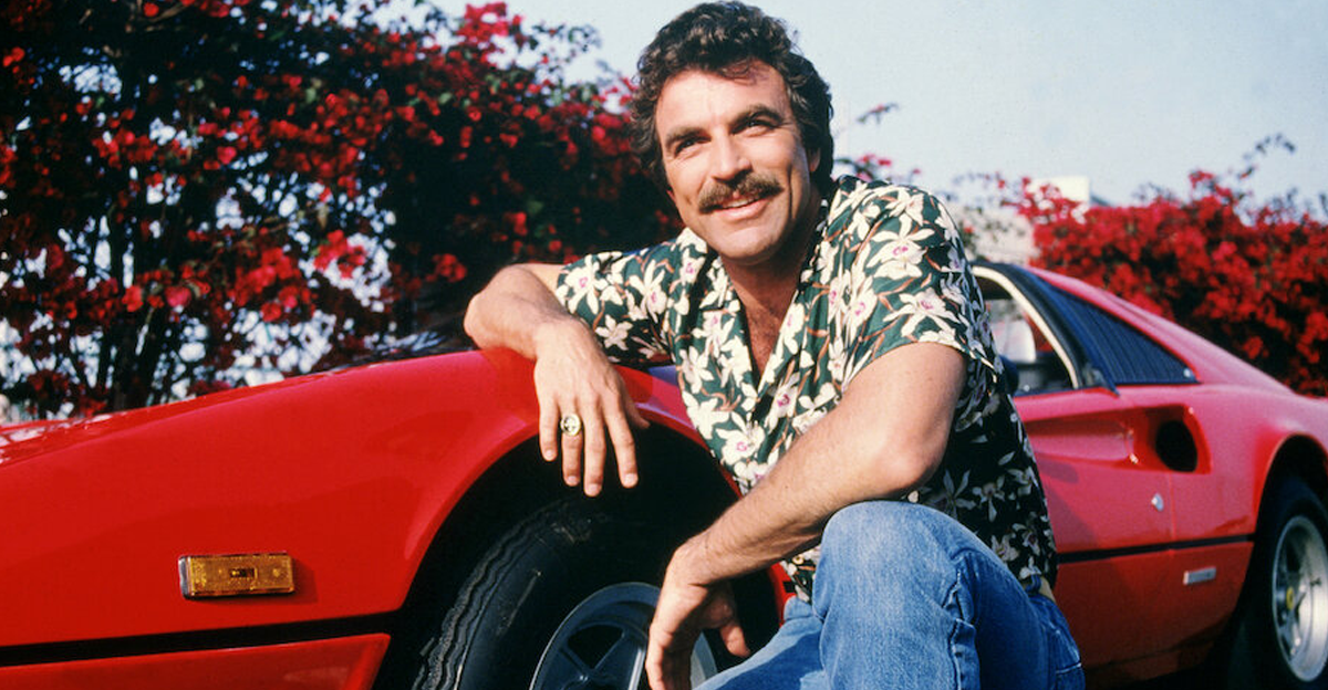 Tom Selleck as the titular investigator in the television series 'Magnum, P.I.', circa 1985. He is posing with his red Ferrari 308