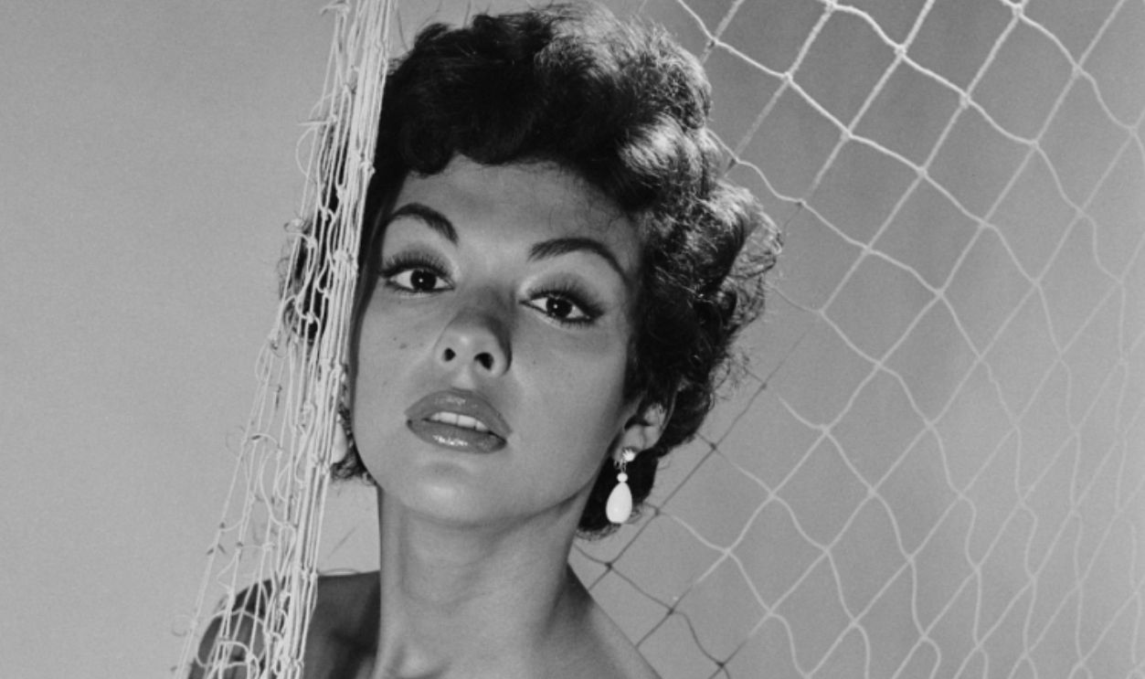 Puerto Rican singer, dancer and actress Rita Moreno, wearing a strapless bathing costume, posing with a fishing net in a studio portrait, circa 1950. (