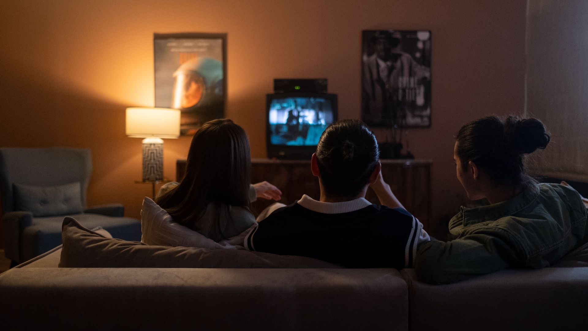 Three people enjoying a relaxed movie night at home, sitting on a couch in a cozy living room.