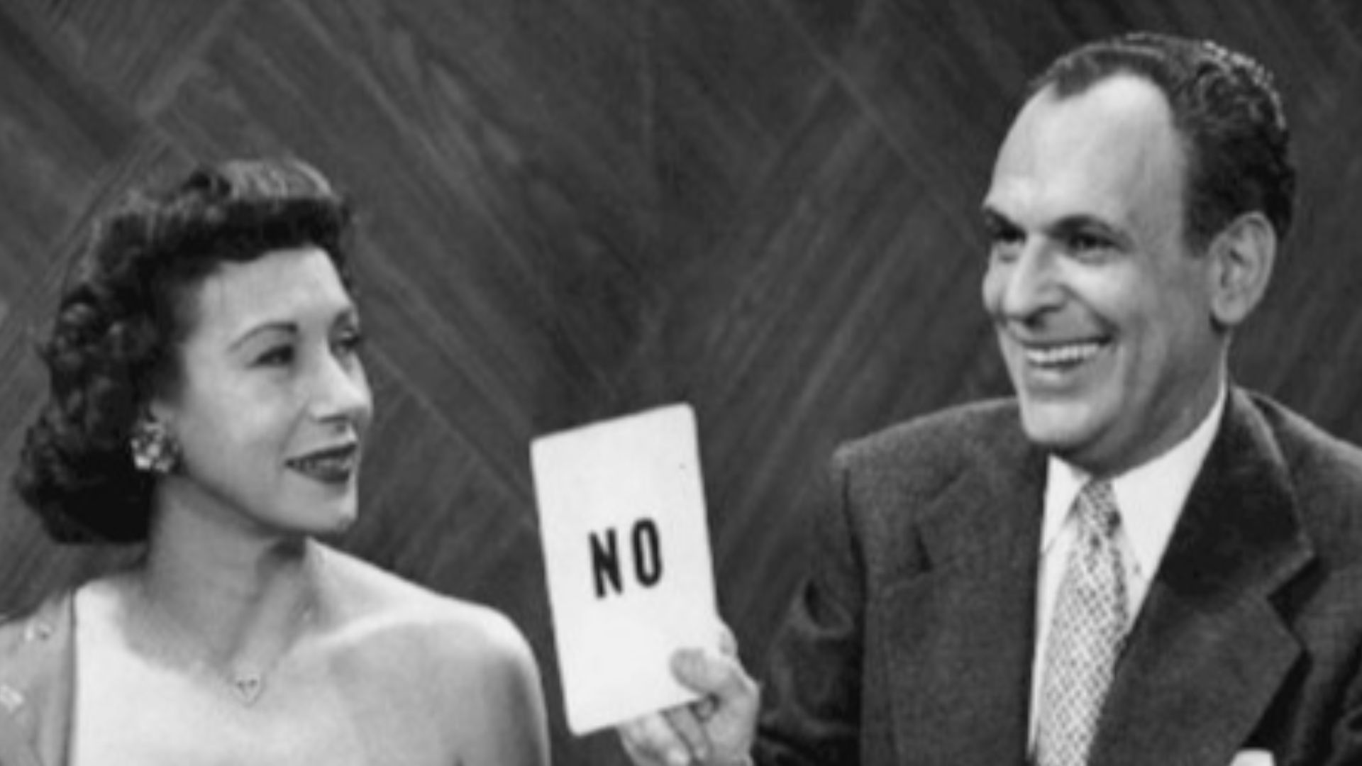 Photo of Arlene Francis and Moss Hart from an early television game show Answer Yes or No.  Panelists tried answering various questions with one of the answer cards.  Hart was the host of the program and is seen revealing Francis' answer to a question.
