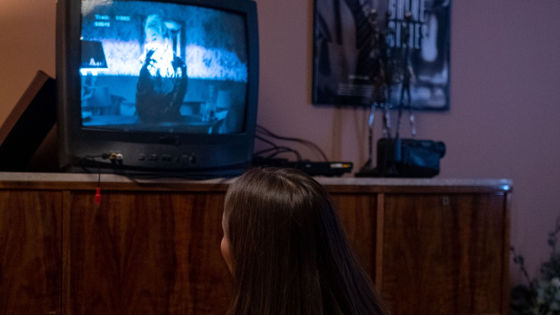 A teenager sits on the floor watching a retro CRT TV in a cozy room.