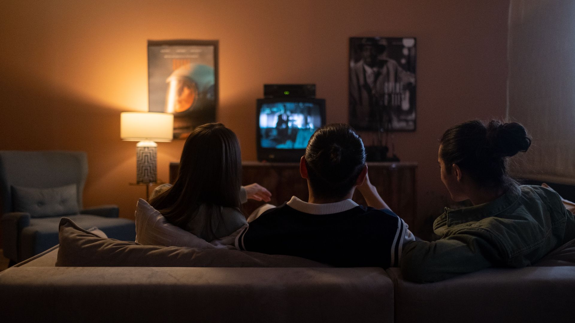 Three people enjoying a relaxed movie night at home, sitting on a couch in a cozy living room.