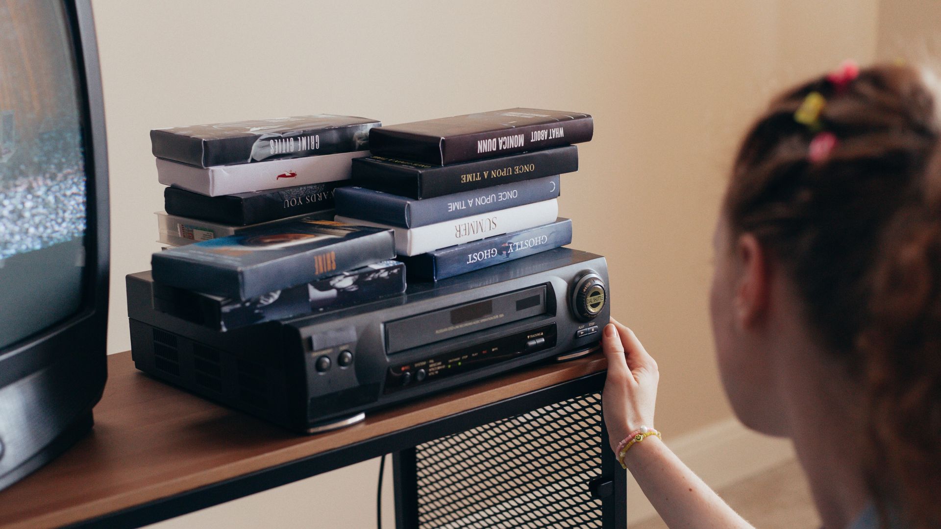 Young woman engaging with retro VHS tapes and a classic VCR setup.