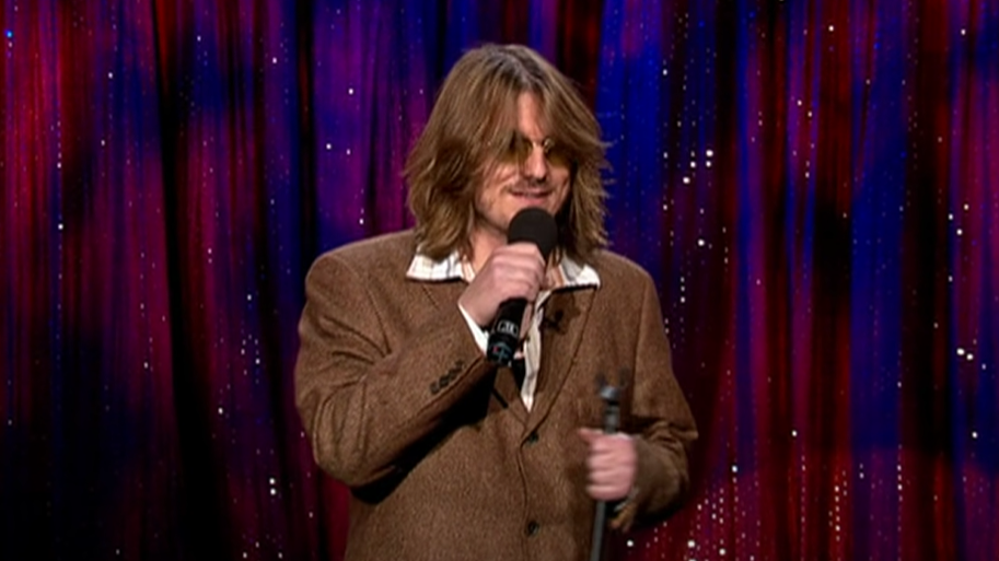 Mitch Hedberg  in brown suit  performing