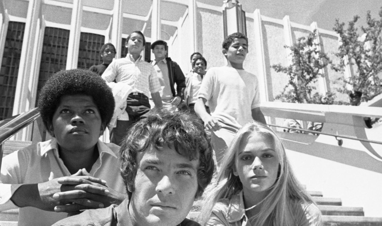 (Original Caption) Los Angeles: Location shooting at the L.A. County Museum of Mod Squad, a television series. (L) Clarence Williams III, (C) Michael Cole, (R) Peggy Lipton, sit while six ghetto boys from New York's lower East side, run down the stair case. The boys appeared as extras in the episode, and were unnamed.