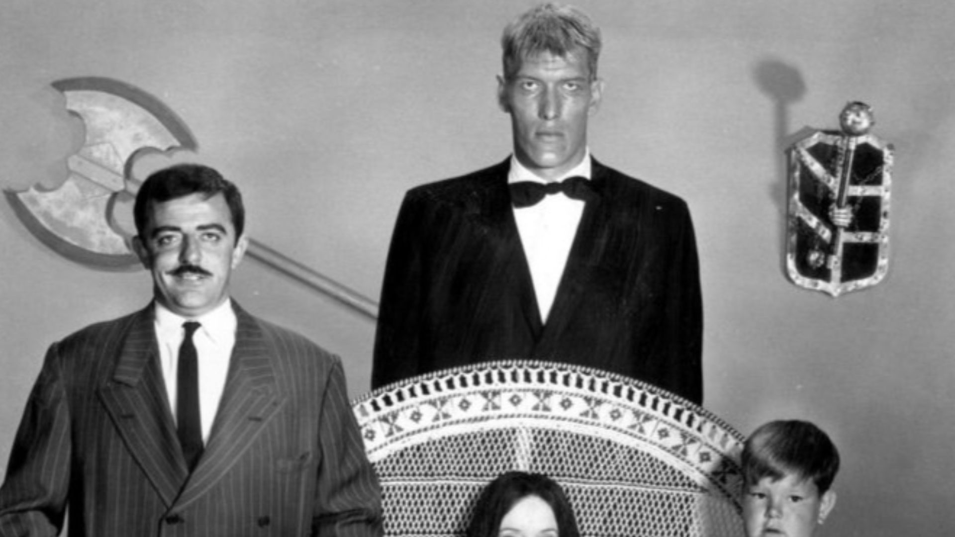 Photo of the main cast of the television program The Addams Family.  Standing back from left—John Astin (Gomez), Ted Cassidy (Lurch).  Standing, front—Lisa Loring (Wednesday), Ken Weatherwax (Pugsley). Seated-Carolyn Jones (Morticia).