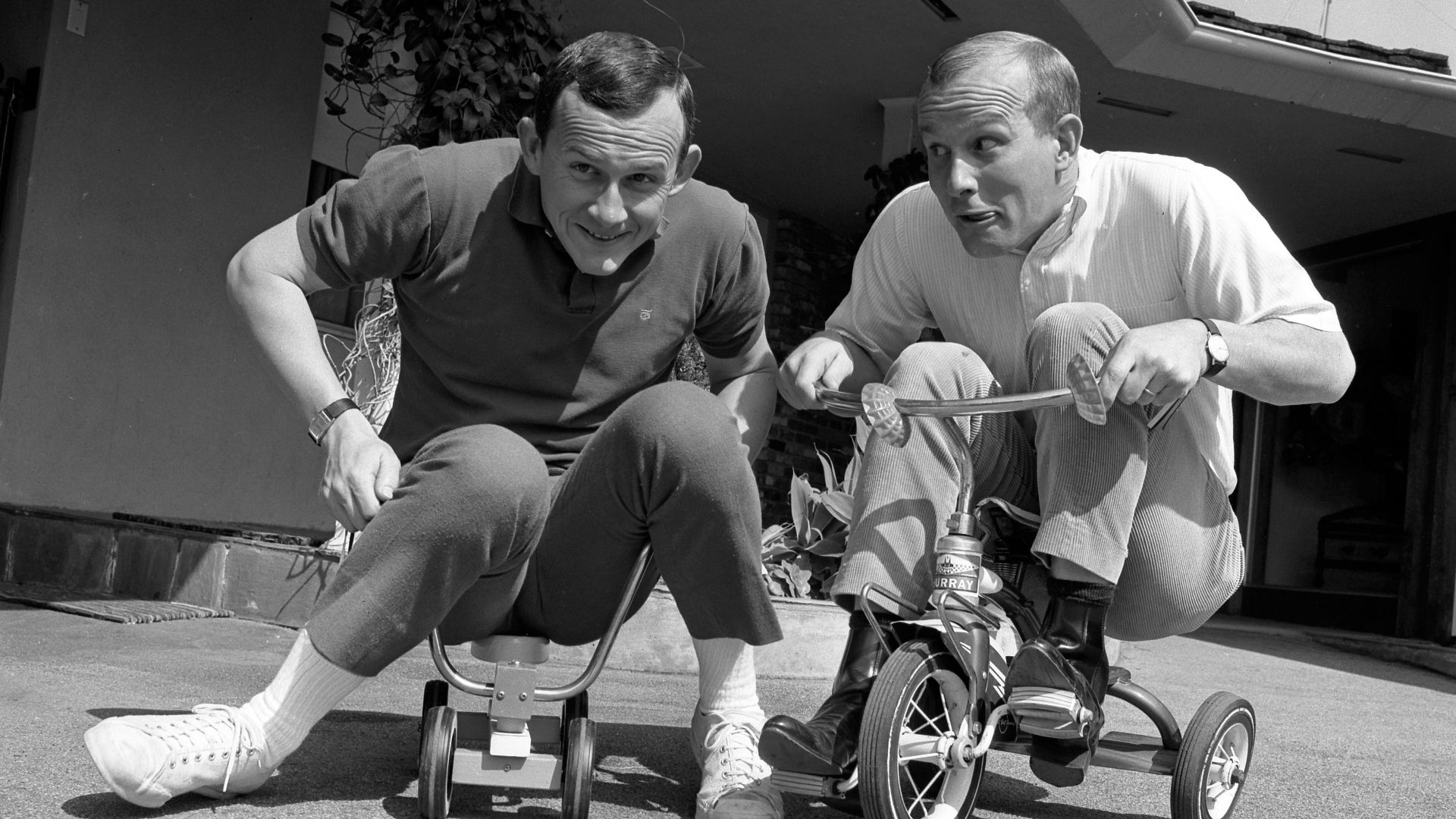 WOULD YOU BELIEVE TWINS?-Dick and Tom Smothers try latest in kiddy transportation as they prepare for appearance Friday at Melodyland. Pat Boone and the Womenfolk will be featured.
