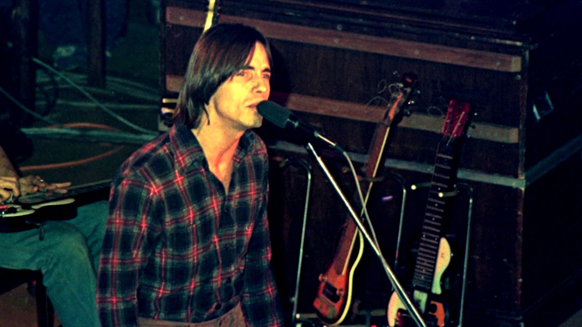 Jackson Browne singing and a partial view of David Lindley playing lap steel guitar in the background