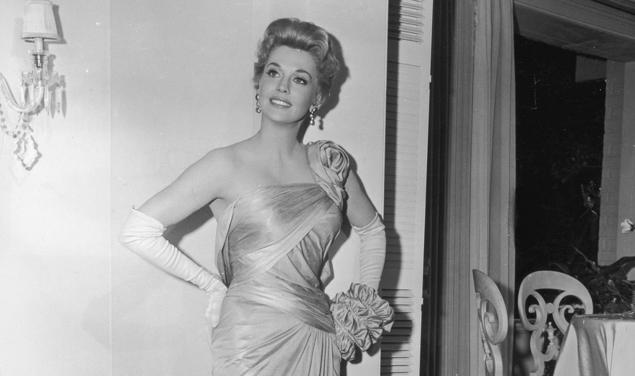 1960: Full-length portrait of American actor Donna Douglas posing in a formfitting, draped, silk gown, designed by Walter Plunkett, while promoting director Vincente Minnelli's film, 'Bells Are Ringing'. 