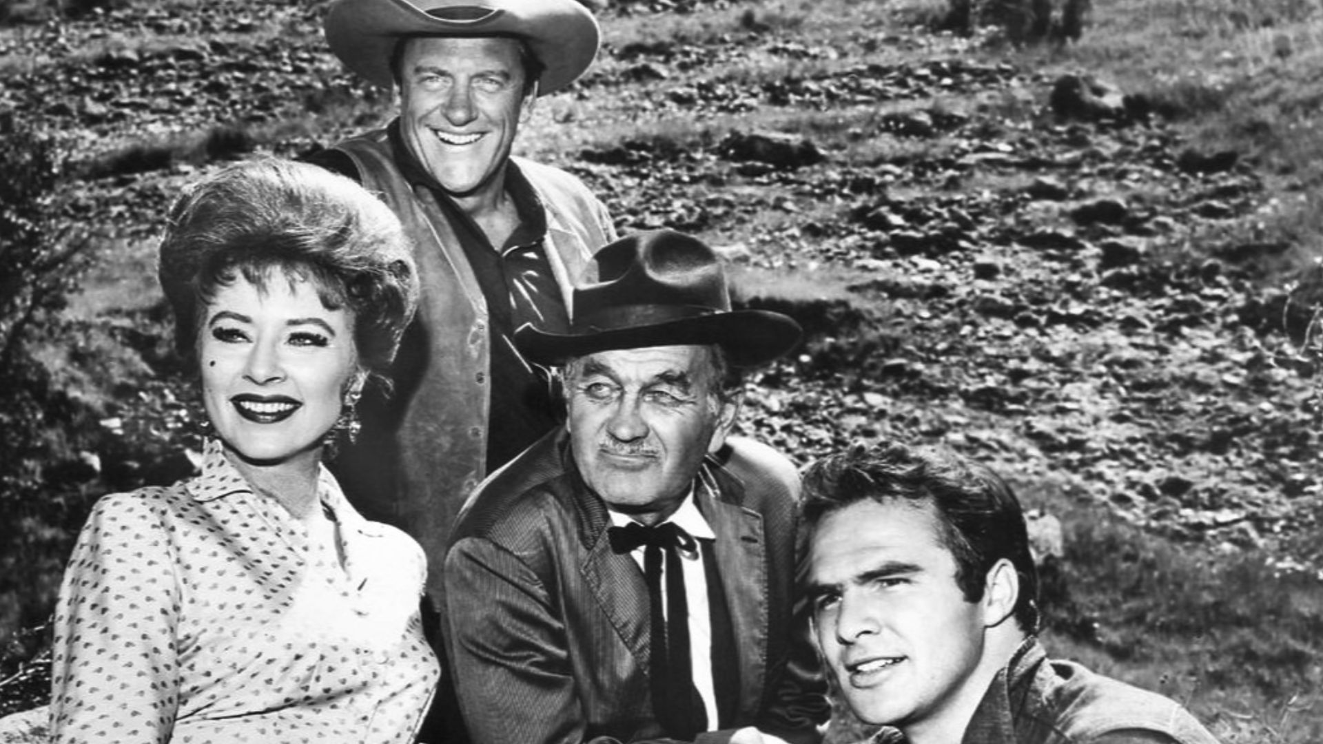 Photo of the main cast for the television program Gunsmoke in 1963.  From left: Amanda Blake (Miss Kitty), James Arness (Matt Dillon), Milburn Stone (Doc Adams), and Burt Reynolds (Quint Asper).