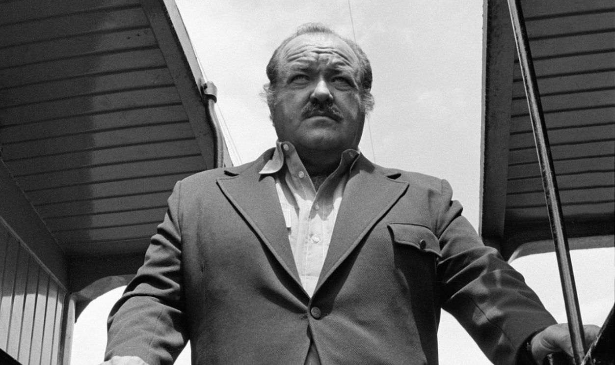Low-angle promotional portrait of American actor William Conrad (1920 - 1994) as he stands between a pair of train cars from an episode of the television drama 'Cannon' entitled 'The Predators,' California, July 24, 1972. The episode was originally broadcast on October 18, 1972.
