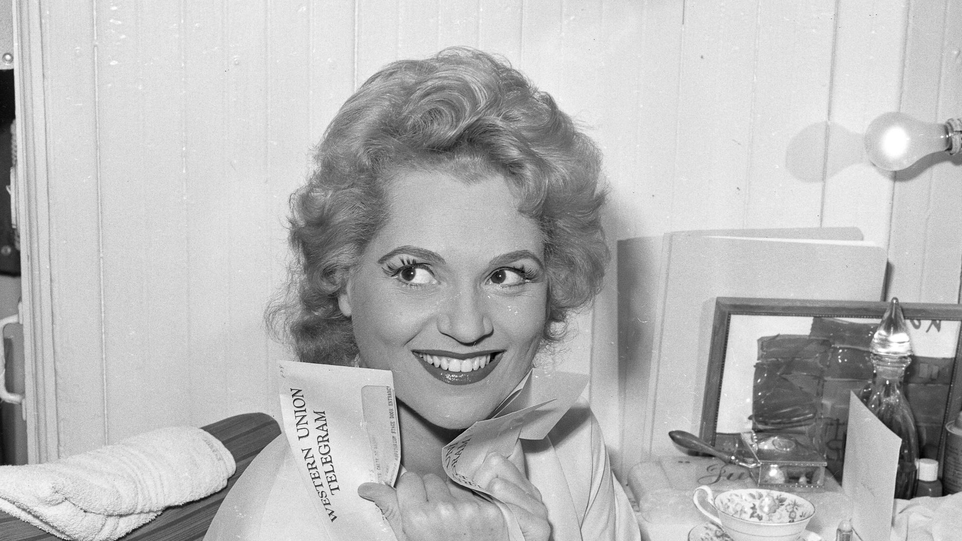 Actress Judy Holliday clutching a telegram in her dressing room before opening of the 22nd season of the Los Angeles Civic Light Opera.
Published caption:STAR OF MUSICAL-- Judy Holliday clutches telegram of good wished in her dressing room before premiere