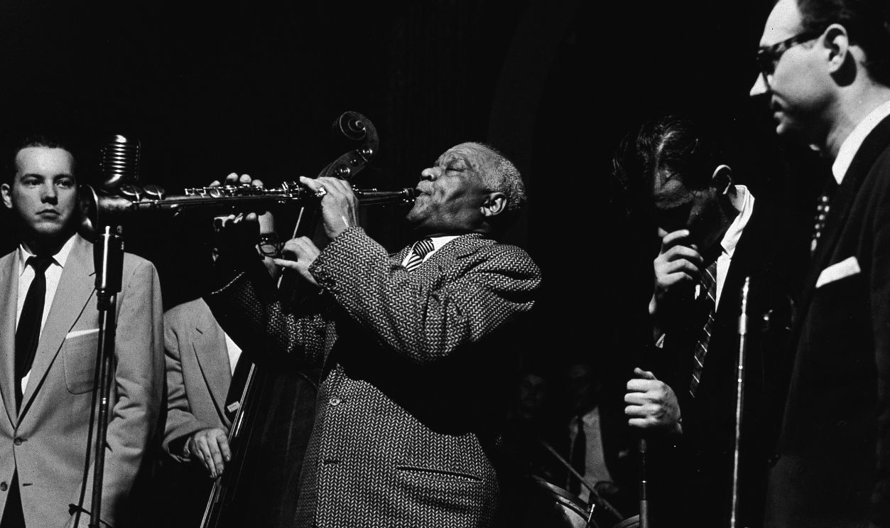Jazz bandleader Sidney Bechet plays soprano saxophone on stage with the Salt City Five and Conrad Janis Bands, 1953. Janis stands at left.