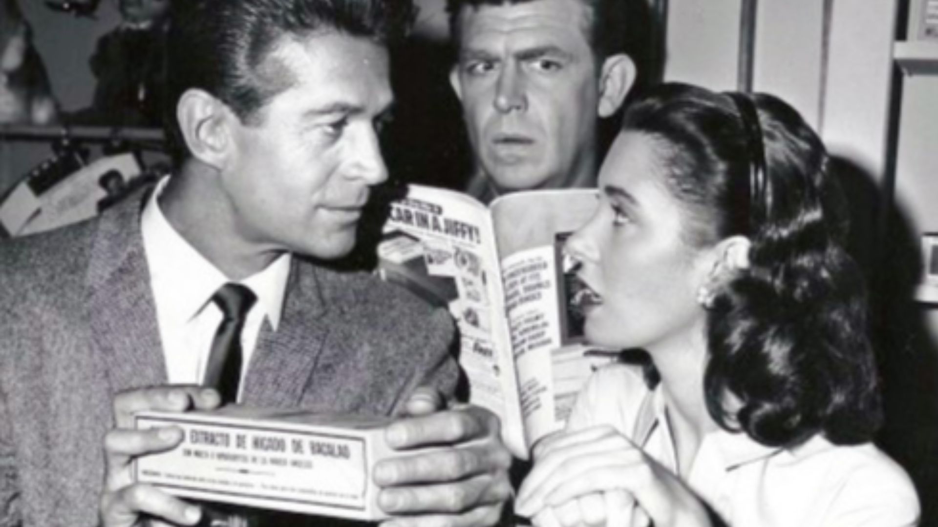 Photo of Andy Griffith, Elinor Donahue and George Nader from the television program The Andy Griffith Show.  Andy can't keep his mind on his magazine as he's trying to hear every word Ellie the pharmacist and Mayberry's new doctor (Nader) are saying.
