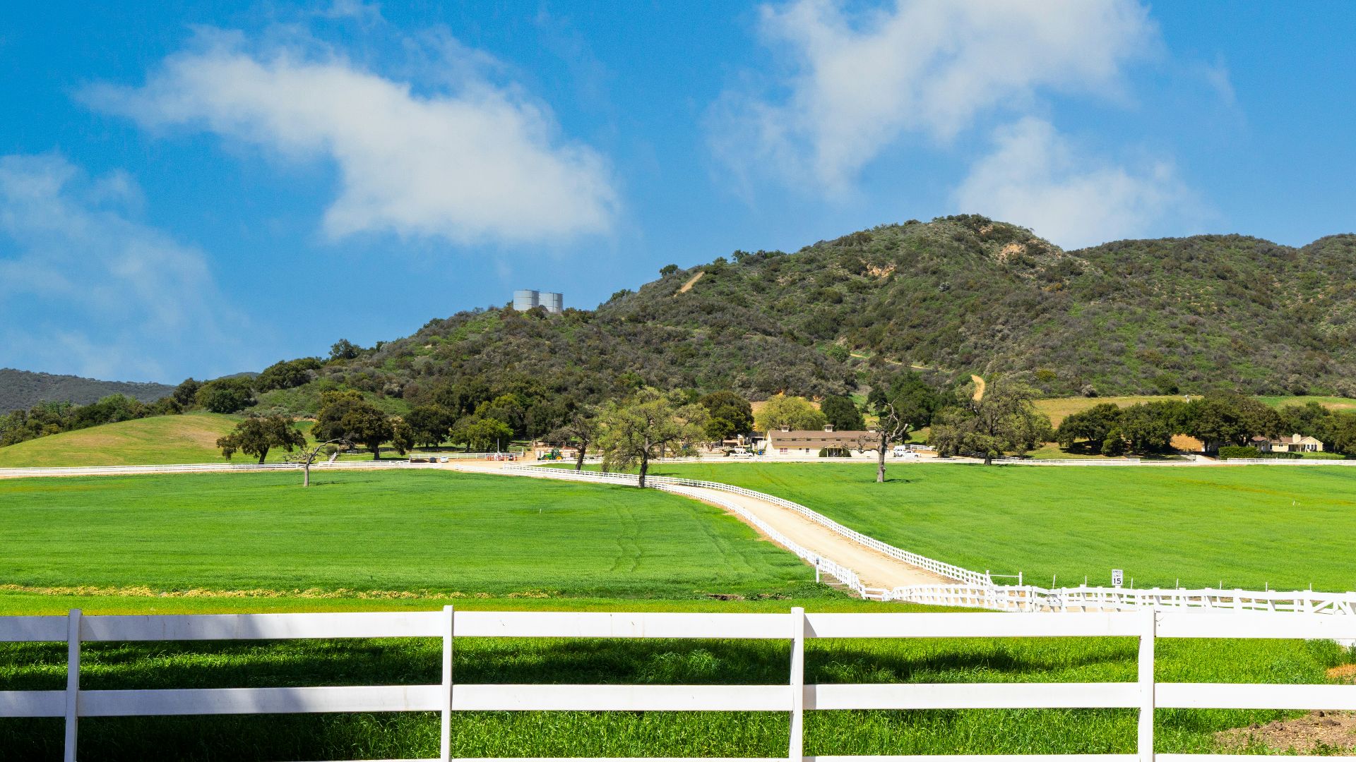 Green fields with a white fence and rolling hills.