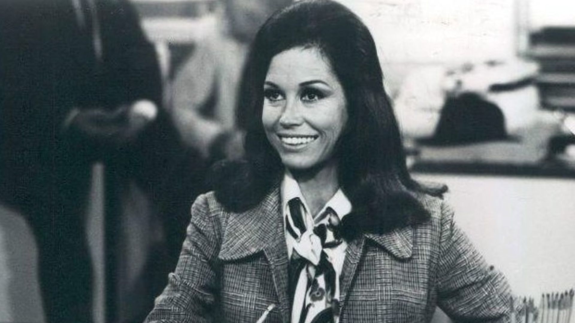 Photo scene from the television program The Mary Tyler Moore Show of Mary Tyler Moore (Mary Richards) at her desk in the WJM-TV newsroom. *Note - this came from a press release dated 1977. The scene is from a 1970 episode.*