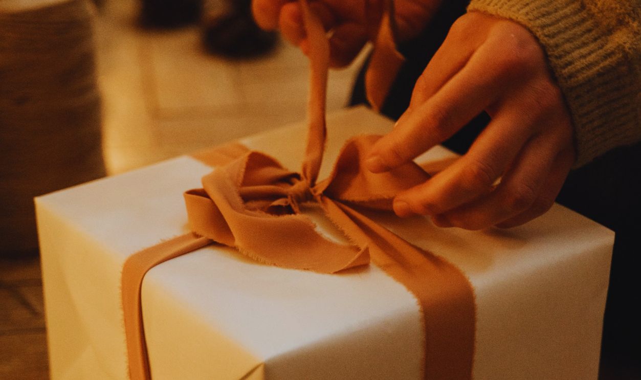 Hands carefully unwrap a gift box with a ribbon in a warm, cozy indoor setting