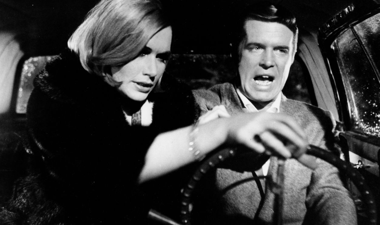 Sally Kellerman grabs the steering wheel as George Peppard tries to keep control in a scene from the Warner Bros. movie 