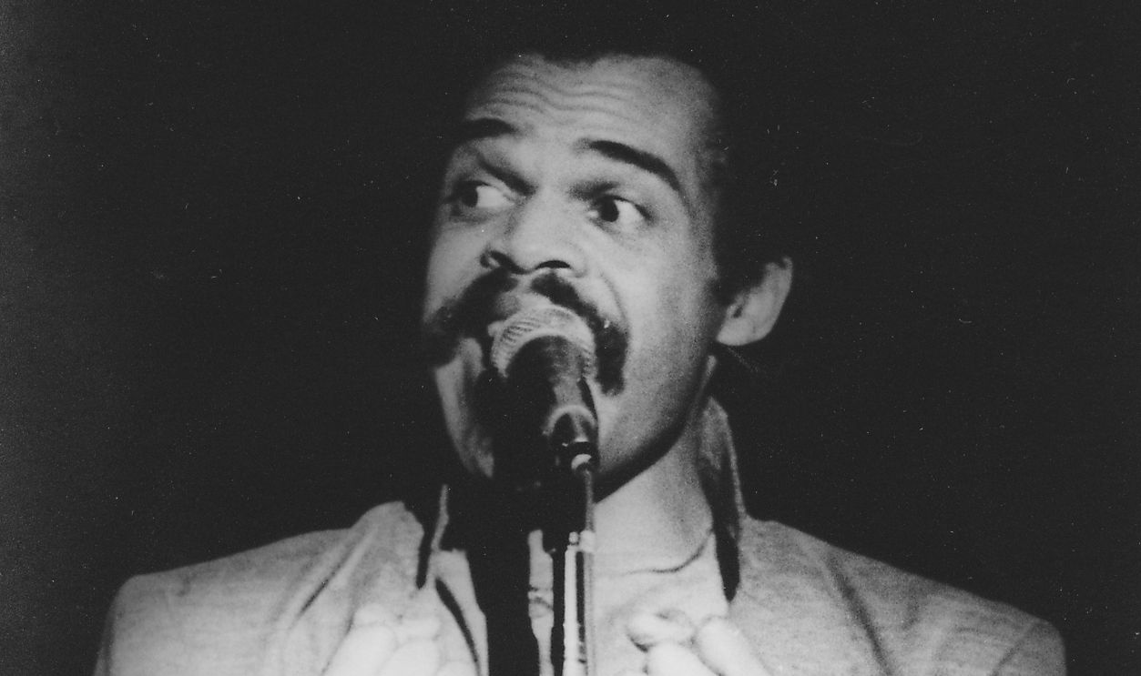 Getty Images - 1369804913 - Mid shot of actor Ted Lange, facing the camera but looking off-frame, speaking into a microphone with his raised hands clenched into fists, California, San Francisco, California, 1995.