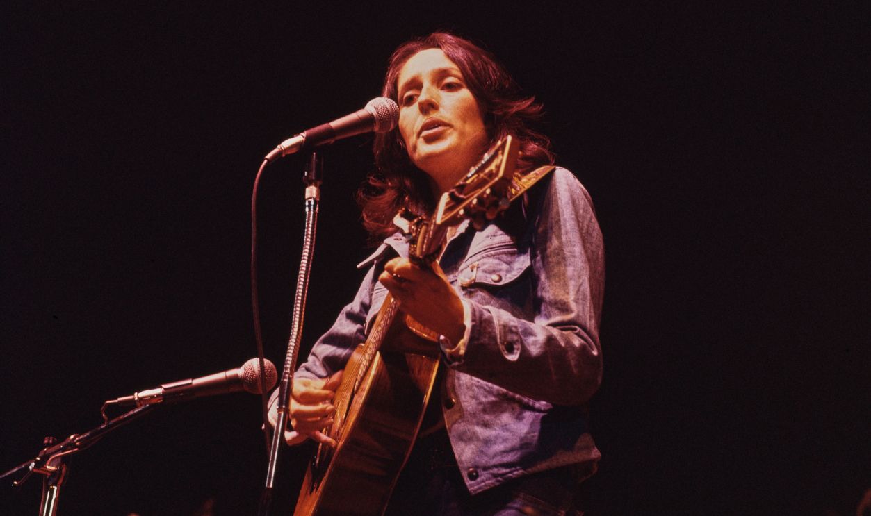American singer-songwriter and guitarist Joan Baez, wearing a denim jacket and playing an acoustic guitar, performing onstage, circa 1975.