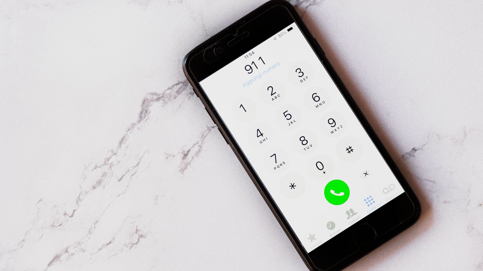Close-up of a smartphone displaying the emergency number 911 on a white marble surface.