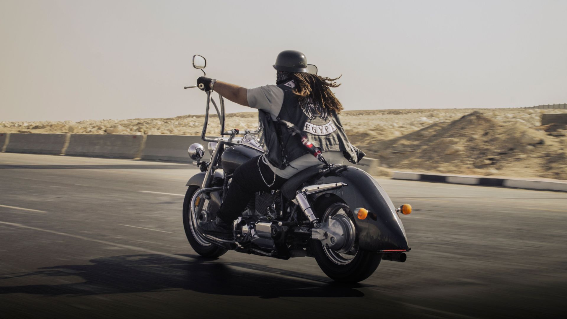 A biker in leather gear riding a motorcycle on a desert highway, embodying freedom.