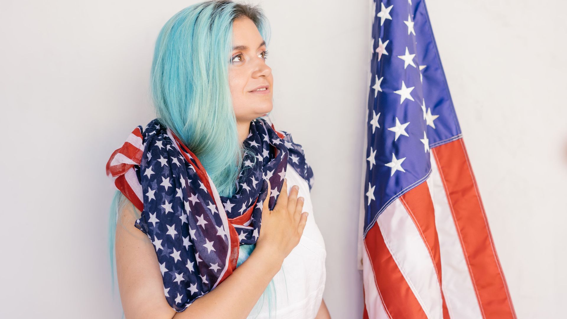 Caucasian woman draped in American flag standing by stars and stripes, showing patriotism.