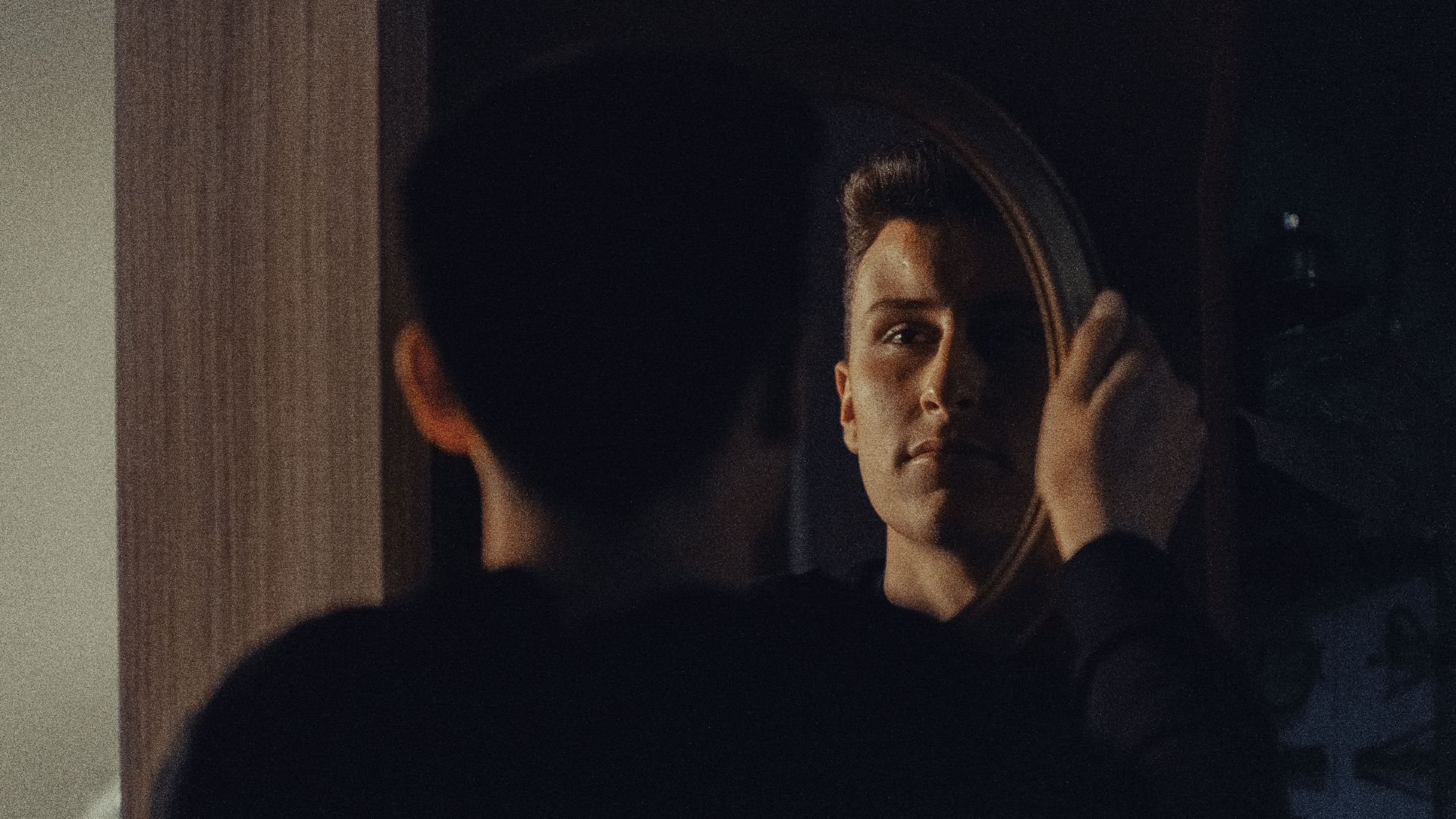 A man gazing at his reflection, capturing an introspective moment indoors.