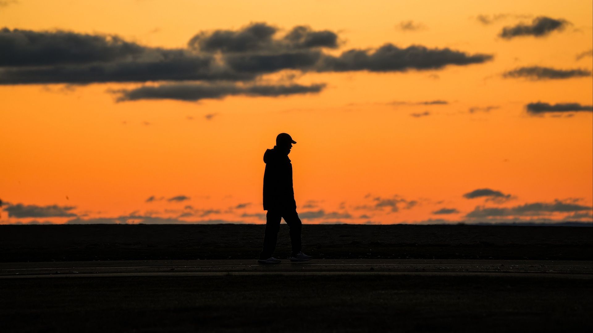 Silhouette of a man walking against a vivid orange sunset sky, creating a dramatic scene.