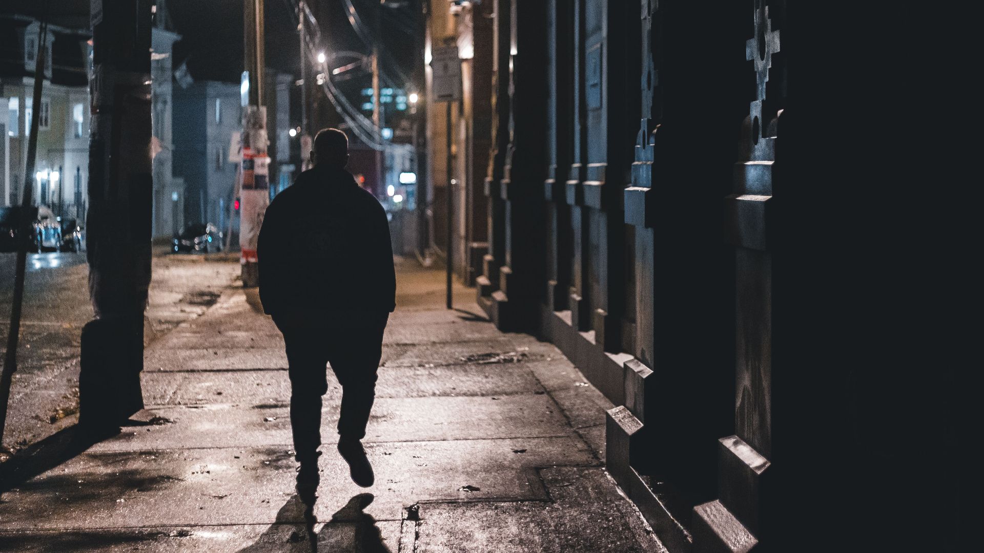 Anonymous silhouette male walking on wet sidewalk on old city street in dark night