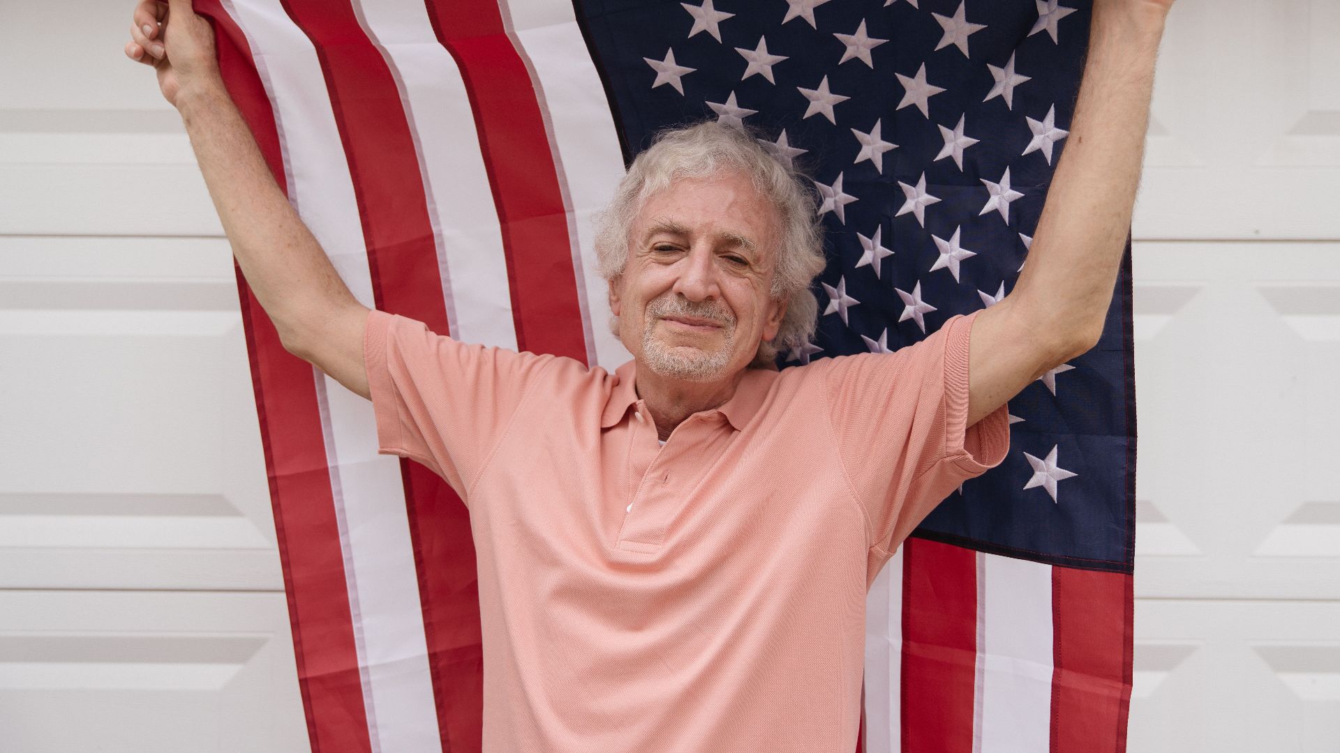 Senior man joyfully holds an American flag, celebrating patriotism and independence.