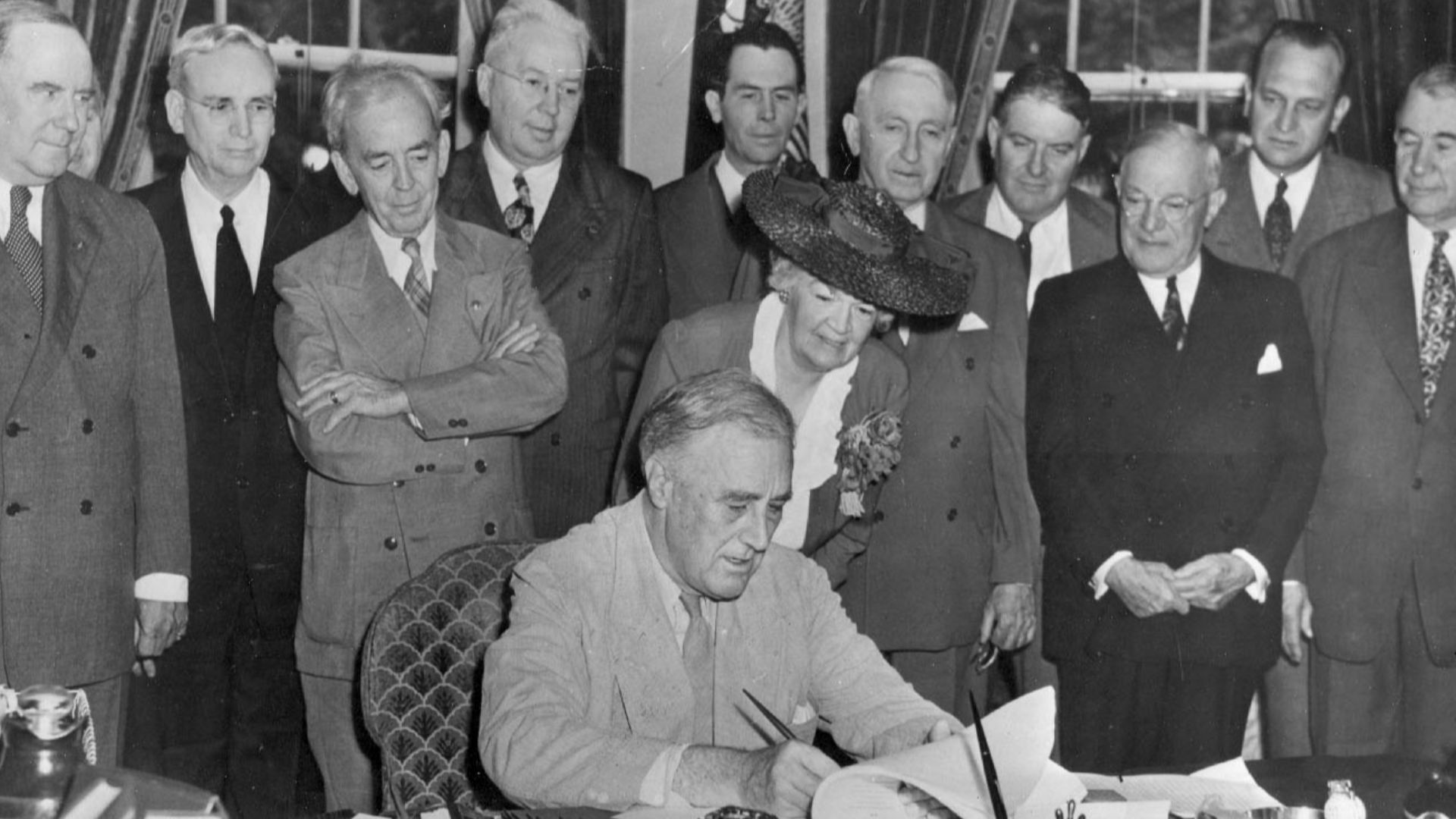 President Franklin D. Roosevelt signs the G.I. Bill in the Oval Office, with (l to r) Bennett “Champ” Clark, J. Hardin Peterson, John Rankin, Paul Cunningham, Edith N. Rogers, J.M. Sullivan, Walter George, John Stelle, Robert Wagner, Scott W. Lucas, and A