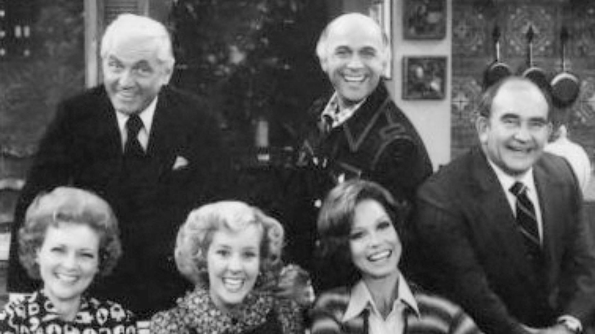 Publicity photo of the cast of The Mary Tyler Moore Show in 1977. From left Standing: Ted Knight (Ted Baxter), Gavin MacLeod (Murray Slaughter), Ed Asner (Lou Grant).  Seated: Betty White (Sue Ann Nivens), Georgia Engel (Georgette Baxter), Mary Tyler Moor