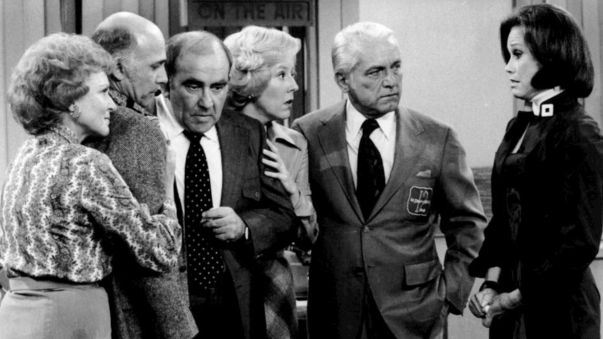 Cast photo from the television program The Mary Tyler Moore Show.  After the news that most of the WJM-TV staff has been fired, everyone gathers in the newsroom.  From left-Betty White (Sue Ann Nivens), Gavin MacLeod (Murray Slaughter), Ed Asner (Lou Gran
