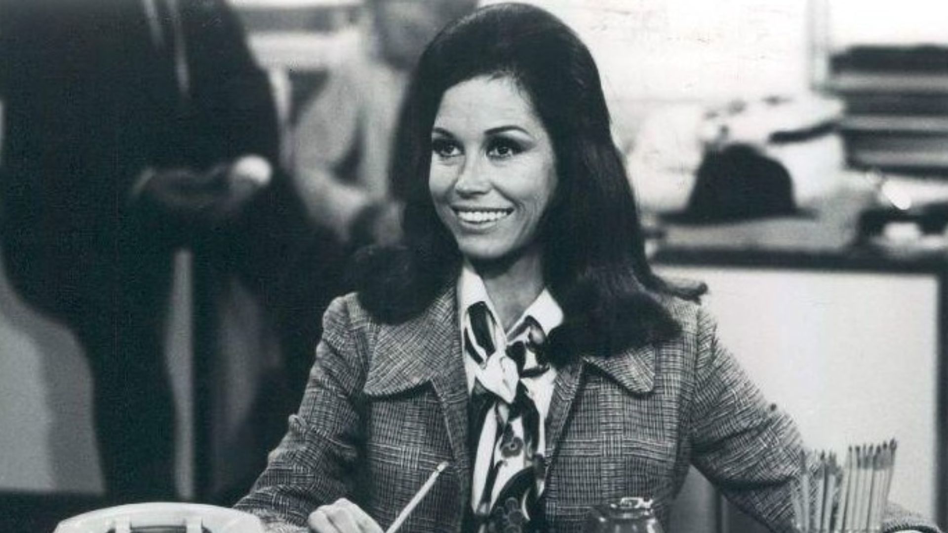 Photo scene from the television program The Mary Tyler Moore Show of Mary Tyler Moore (Mary Richards) at her desk in the WJM-TV newsroom. *Note - this came from a press release dated 1977. The scene is from a 1970 episode.*