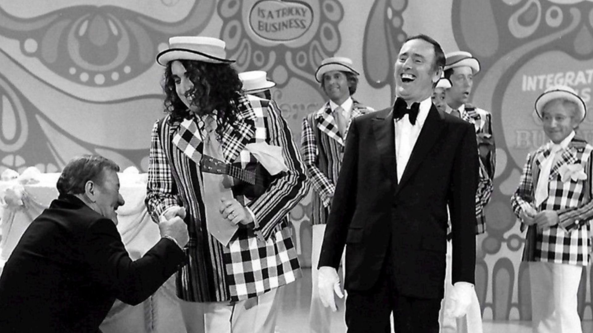 Publicity photo from the 100th episode of the television program Rowan & Martin's Laugh-In.  Guest stars are John Wayne and Tiny Tim. Host Dick Martin is pictured, along with past and present cast members from the show.  Visible in the background are Ruth