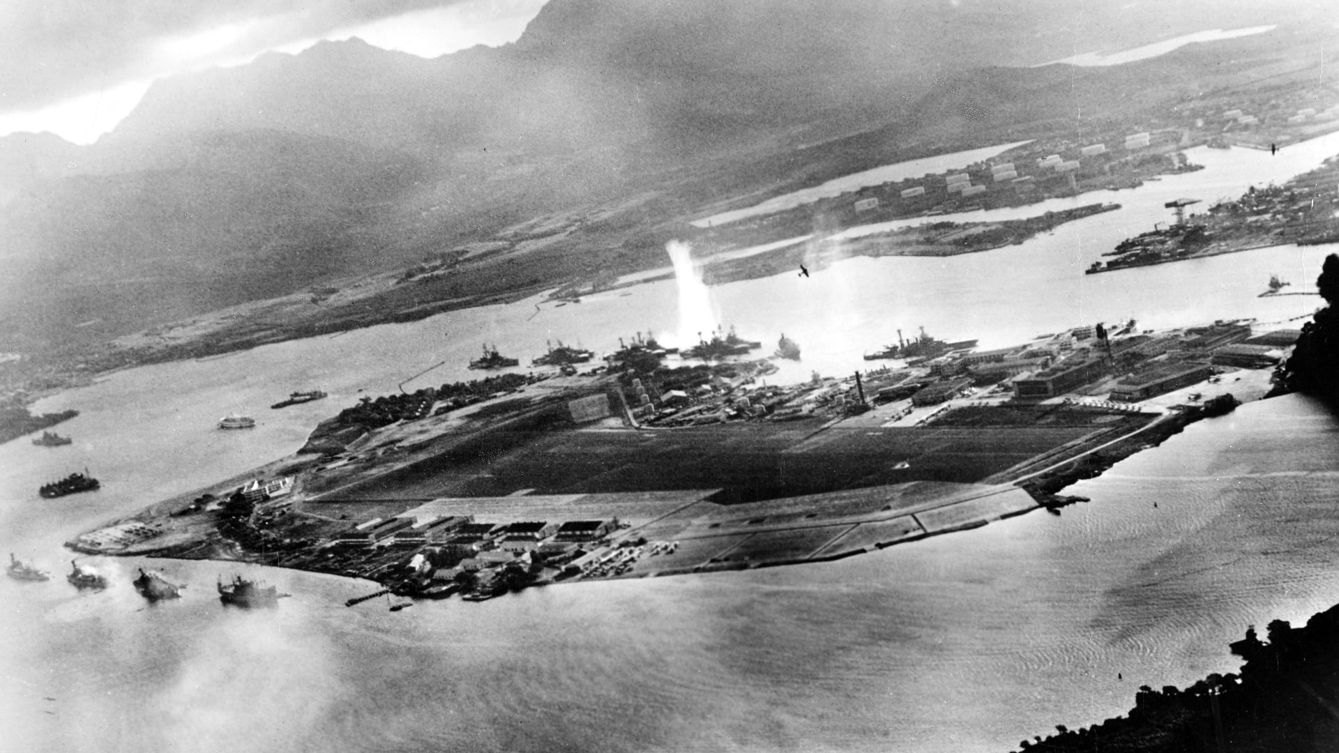 Photograph taken from a Japanese plane during the torpedo attack on ships moored on both sides of Ford Island shortly after the beginning of the Pearl Harbor attack. View looks about east, with the supply depot, submarine base and fuel tank farm in the ri