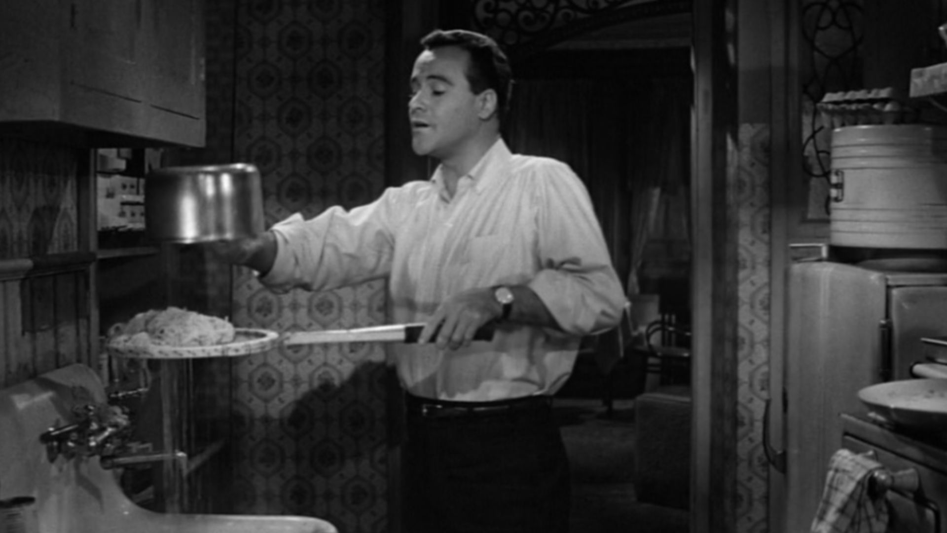Screenshot of Jack Lemmon as C.C. Baxter using a tennis racket to strain spaghetti in the trailer for the film The Apartment (1960)
