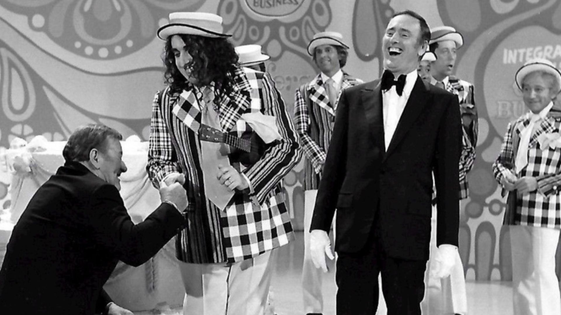 Publicity photo from the 100th episode of the television program Rowan & Martin's Laugh-In.  Guest stars are John Wayne and Tiny Tim. Host Dick Martin is pictured, along with past and present cast members from the show.  Visible in the background are Ruth