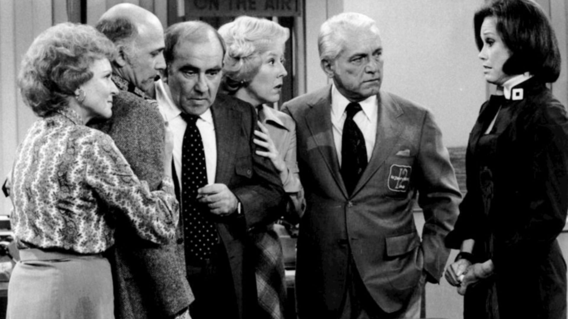 Cast photo from the television program The Mary Tyler Moore Show.  After the news that most of the WJM-TV staff has been fired, everyone gathers in the newsroom.  From left-Betty White (Sue Ann Nivens), Gavin MacLeod (Murray Slaughter), Ed Asner (Lou Gran