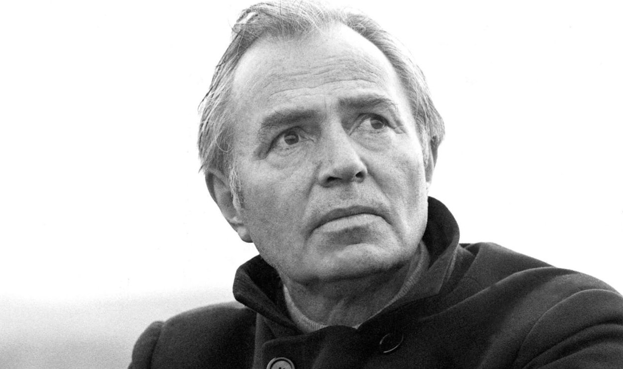 James Mason (1909-1984), British actor, wearing a black overcoat, leaning on a dry stone wall, circa 1970. 