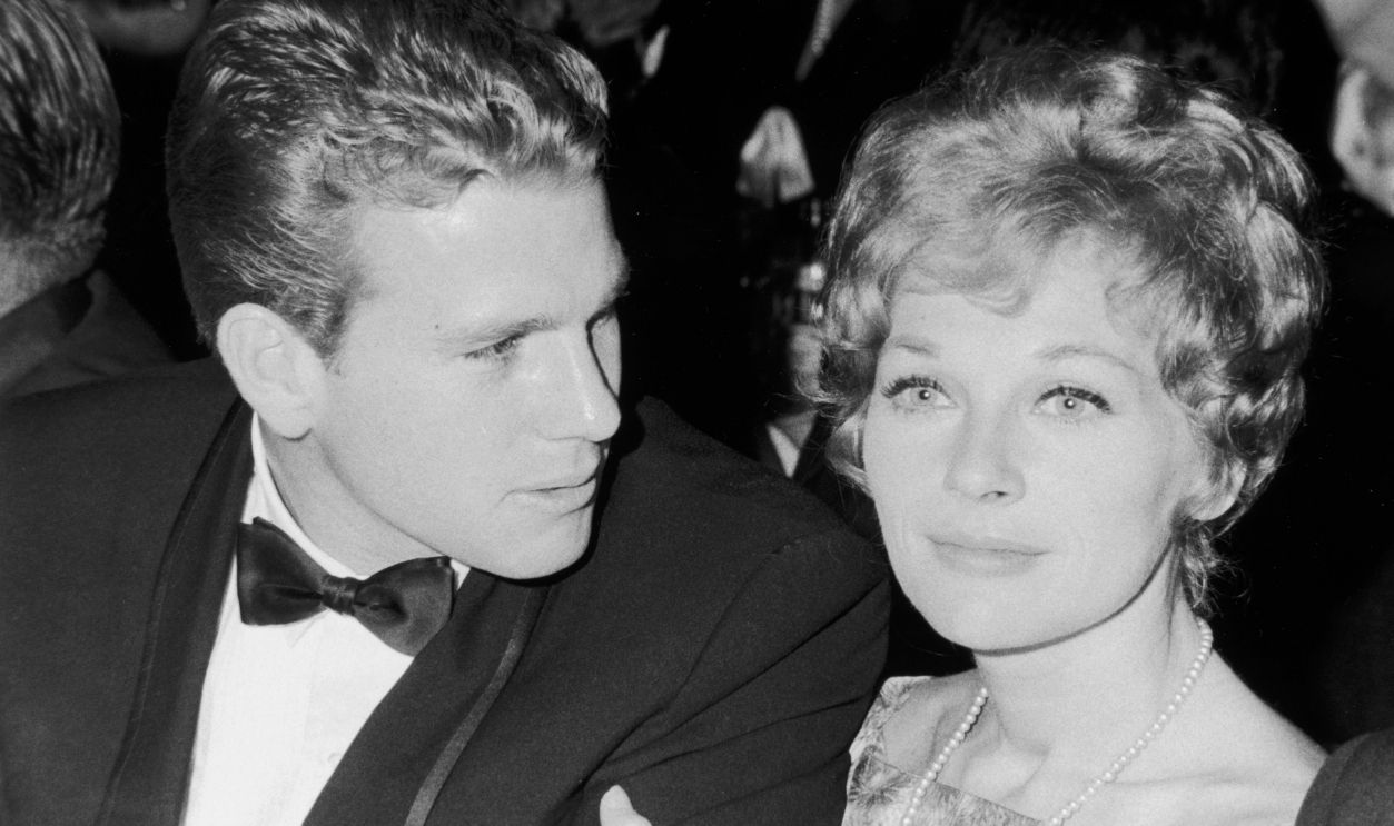 Married American actors Ryan O'Neal and Joanna Moore (1934 - 1997) at a Hollywood event, California. Moore has her arm wrapped around O'Neal's as he speaks to her.