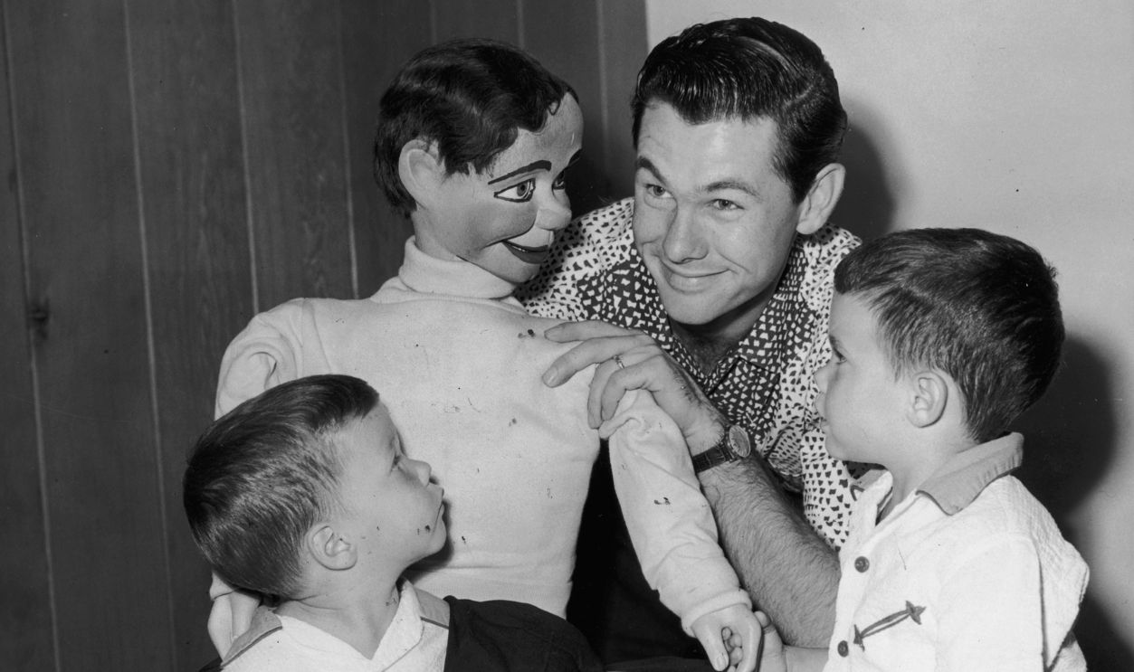 American comedian and television show host Johnny Carson (1925 - 2005) (top) plays with a ventriloquist's dummy, as his sons, Ricky and Kit, look on.