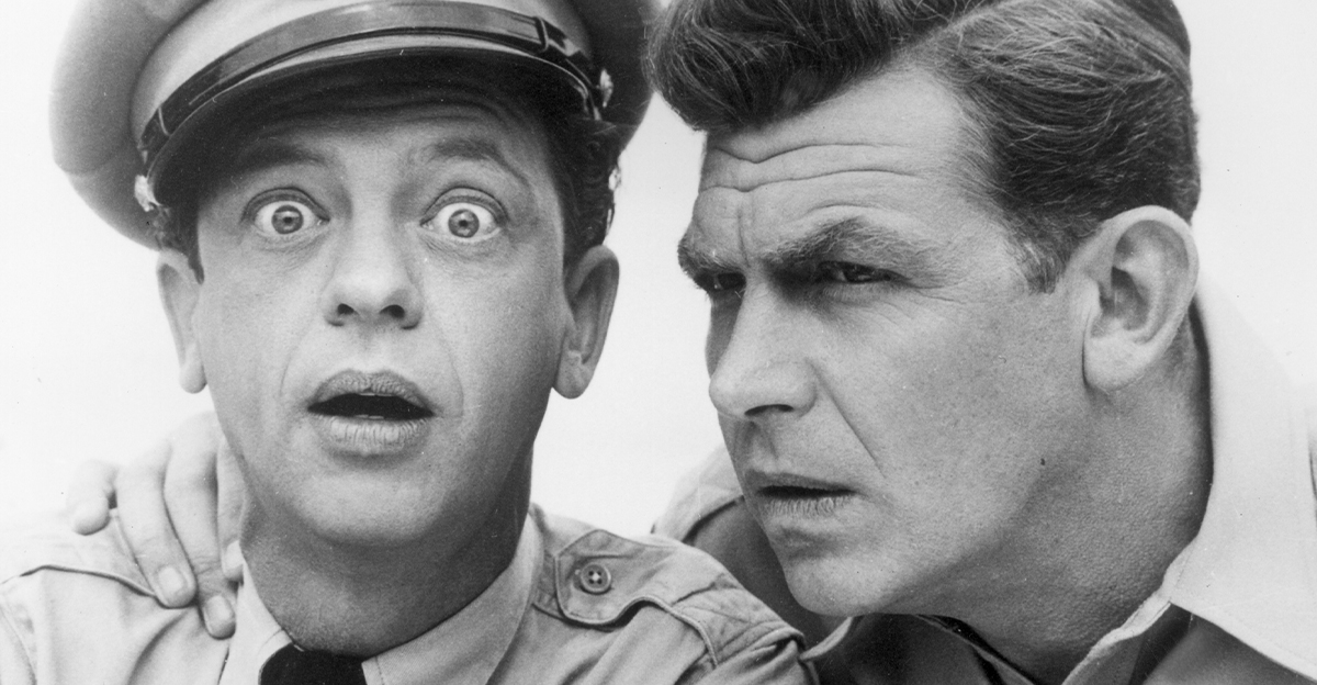 American actor Don Knotts looks at the camera with a surprised expression, as Andy Griffith holds his hand on his shoulder, posing in character as Deputy Barney Fife and Sheriff Andy Taylor