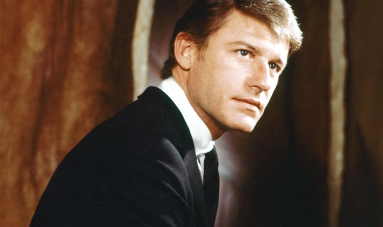 Roddy McDowall (1928-1998), British actor, wearing a black suit, with a white shirt and black tie, and holding a lit cigarette in a studio portrait, circa 1965. (