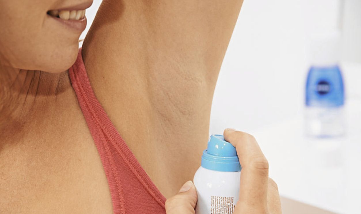 Woman applying spray deodorant.