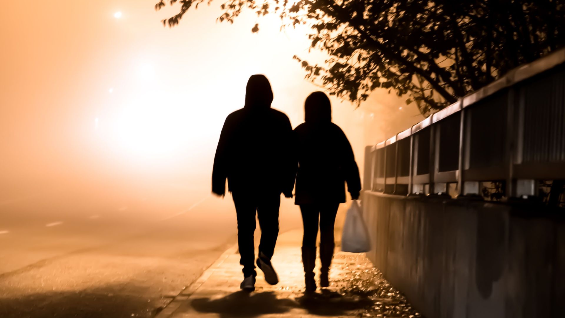 A silhouette of a couple holding hands, walking on a foggy night in Toronto, Canada.