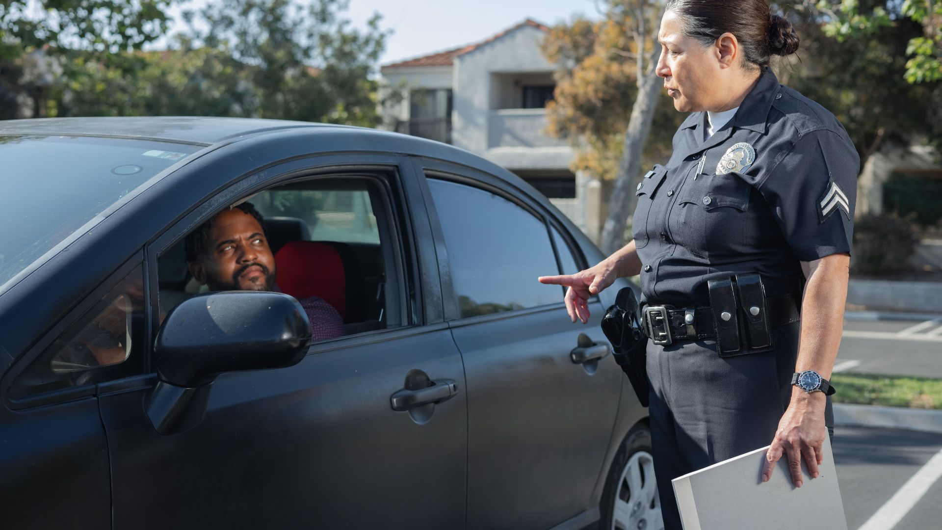 A police officer interacts with a driver during a daytime traffic stop on a residential street.