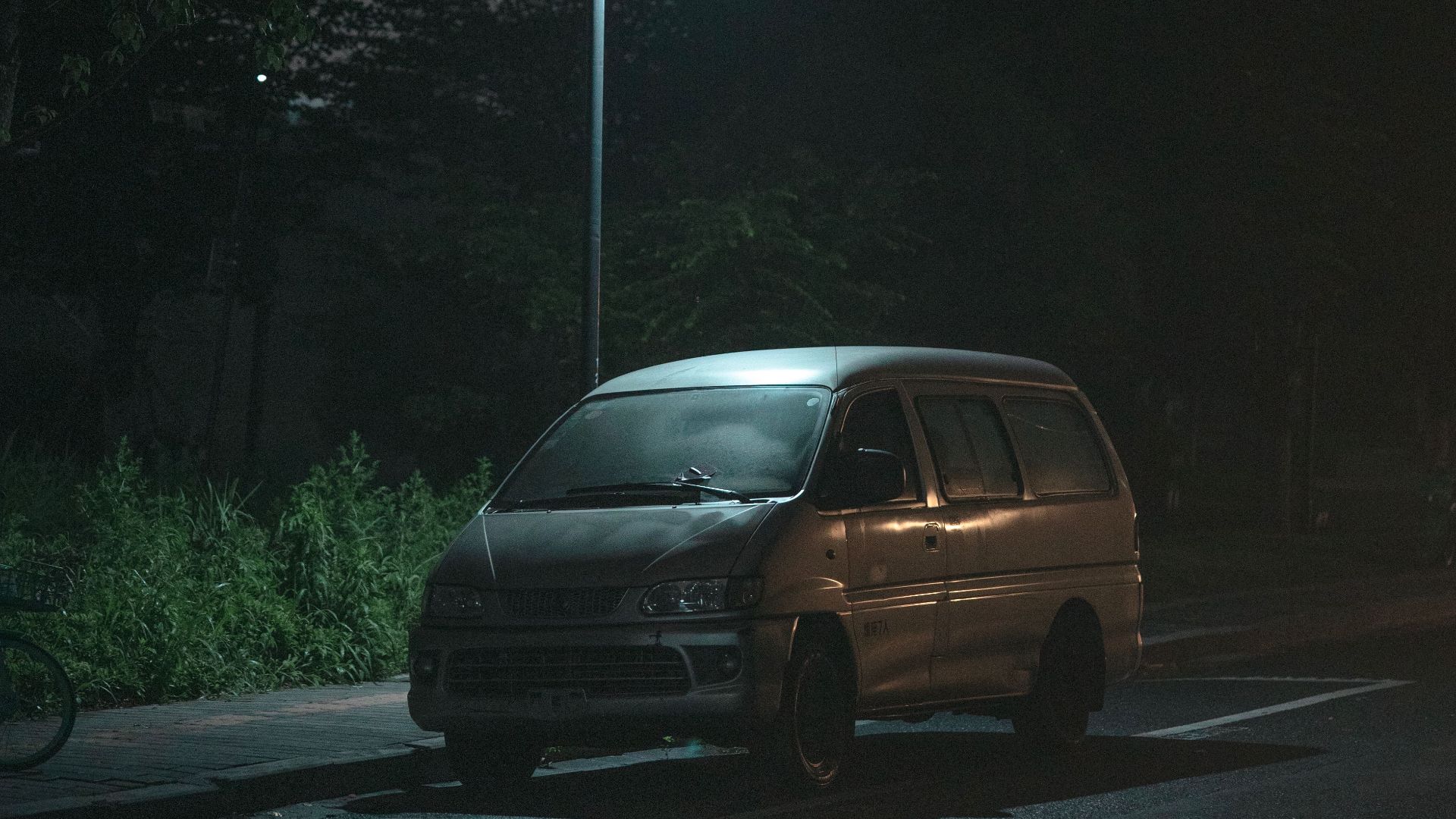 A moody night scene of a van parked under a streetlamp, evoking solitude.