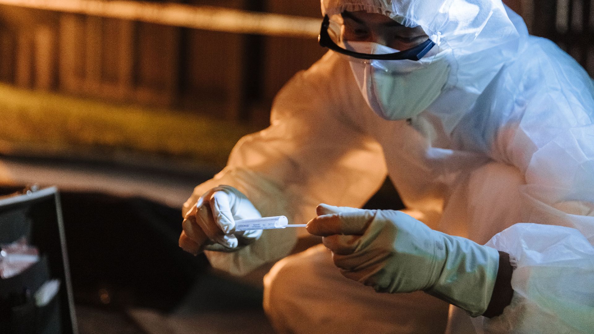 A forensic investigator in protective gear collects evidence outdoors at night.